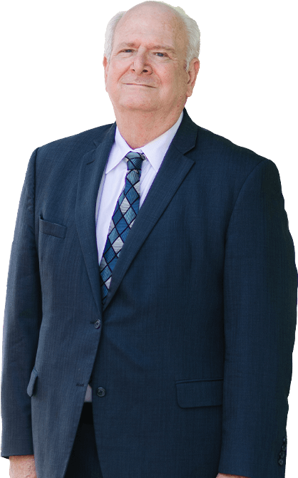 A man with dark hair and a beard, wearing a dark striped suit, light blue shirt, and pink tie, stands smiling with one hand in his pocket. A man with dark hair and a beard, wearing a dark striped suit, light blue shirt, and pink tie, stands smiling with one hand in his pocket.