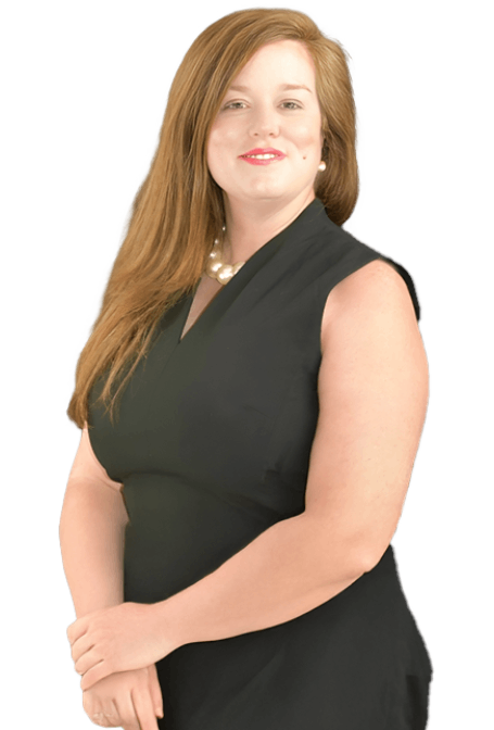 A woman with long brown hair wearing a sleeveless black dress and a pearl necklace stands smiling with her hands clasped in front of her against a white background. A woman with long brown hair wearing a sleeveless black dress and a pearl necklace stands smiling with her hands clasped in front of her against a white background.