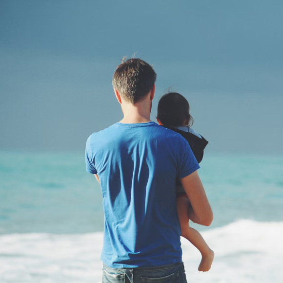 A woman and a man sit closely with a young girl between them. The adults appear comforting and supportive as the girl looks down with a thoughtful expression. The scene suggests a caring family moment.