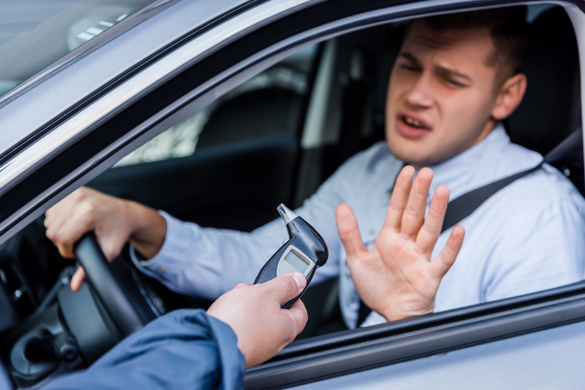 A man in a car holds up his hand, refusing to take a breathalyzer test offered by a person standing outside the vehicle. A man in a car holds up his hand, refusing to take a breathalyzer test offered by a person standing outside the vehicle.