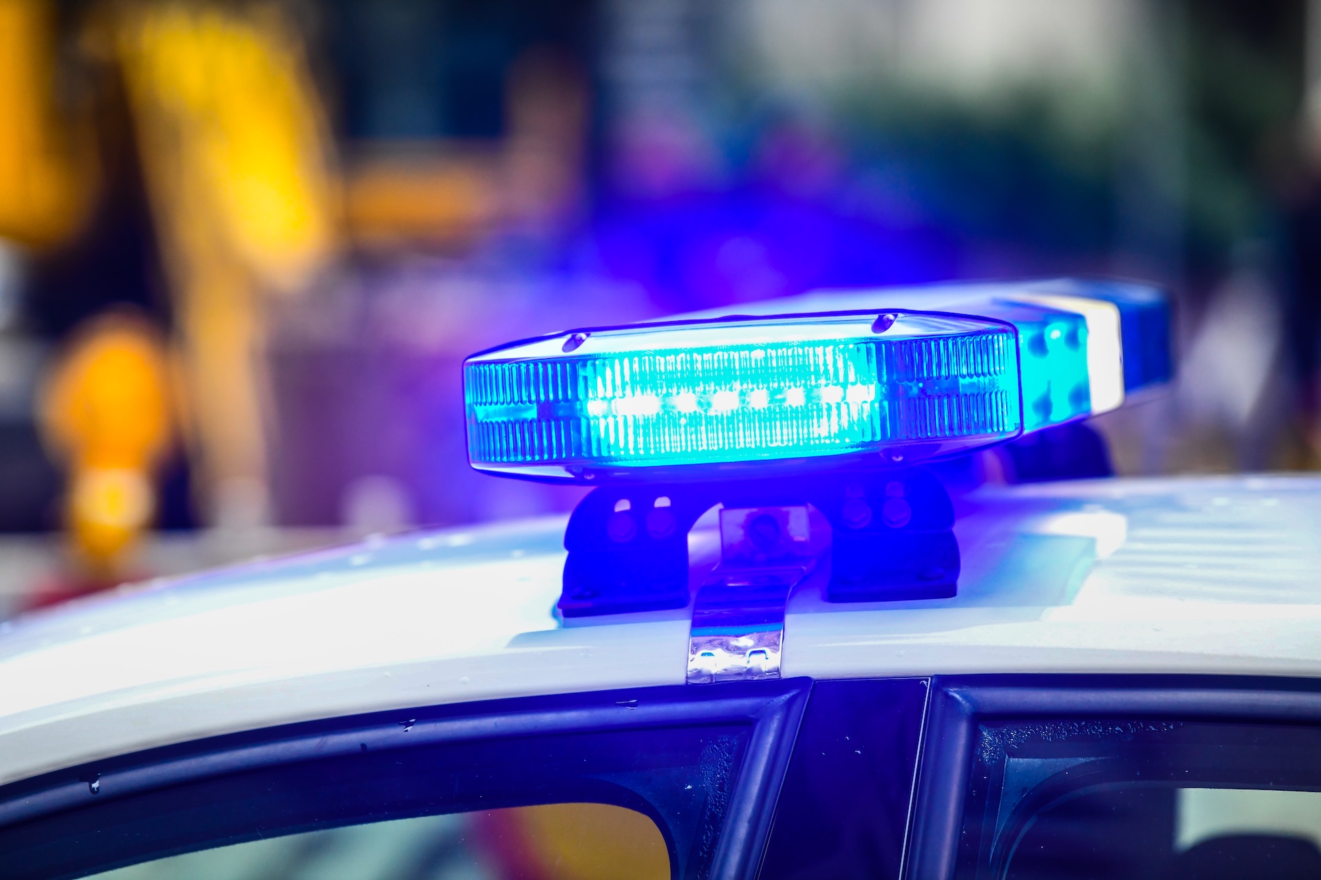 Close-up of a blue emergency police siren light flashing on top of a white police car, with a blurred background of outdoor surroundings. Close-up of a blue emergency police siren light flashing on top of a white police car, with a blurred background of outdoor surroundings.